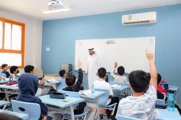 عرض تقديمي عن غياب المعلمات وتأثيرة علي العمل ويظهر معلم يقف في مقدمة فصل دراسي ، ويتفاعل مع مجموعة من الطلاب الجالسين على مقاعد دراسية.